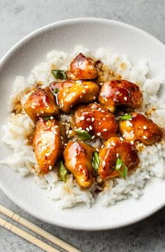 a white bowl filled with rice and chicken on top of it next to chopsticks