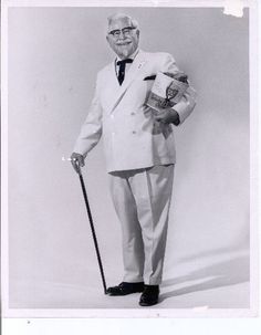 an old man in a white suit holding a book and a cane, posing for a black and white photo