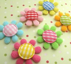 four different colored felt flowers on a polka dot tablecloth with green, pink, blue and yellow dots