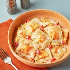 a bowl filled with ravioli and cheese on top of an orange napkin next to two salt shakers