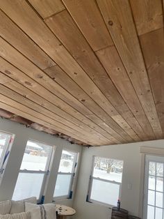 a living room filled with furniture and windows covered in wood planks on the ceiling