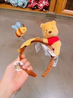 a hand holding a winnie the pooh bear toy with two bees on it's back