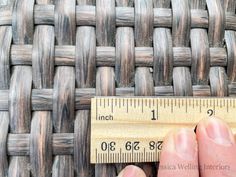 a person holding a ruler in front of a woven piece of wood with the measuring tape on it