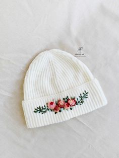 a white beanie with flowers on it sitting on top of a bed next to a pillow