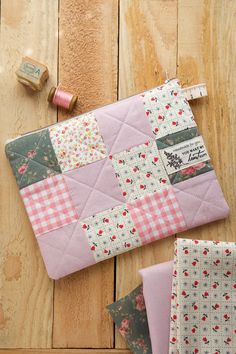 pink and white patchwork quilts on wooden floor next to sewing needle, thread and spool