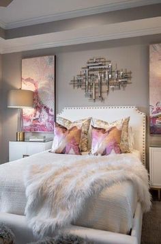 a white bed topped with lots of pillows next to a wall mounted art piece in a bedroom