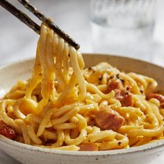 a bowl of noodles with chopsticks sticking out of the top, on a table