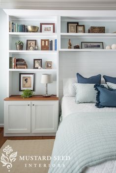 a bed with blue pillows and white bookcases next to a wall mounted bookshelf