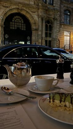 a table topped with plates and cups filled with food next to a black car parked in front of a building