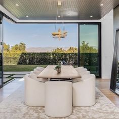 a dining room table surrounded by white chairs in front of an open patio with sliding glass doors