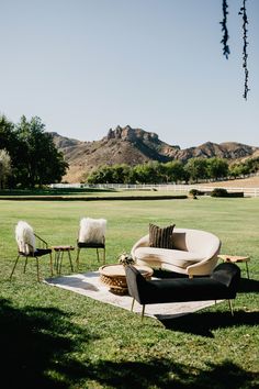 two chairs and a couch in the middle of a grassy field with mountains in the background