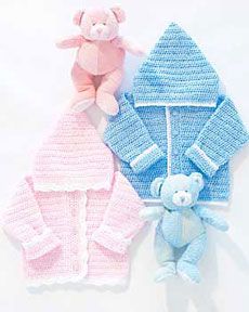 three knitted sweaters and a teddy bear sitting next to each other on a white surface