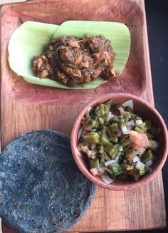 a wooden tray topped with food next to a tortilla