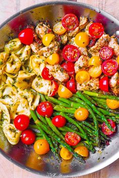 a pan filled with chicken, asparagus, tomatoes and other veggies