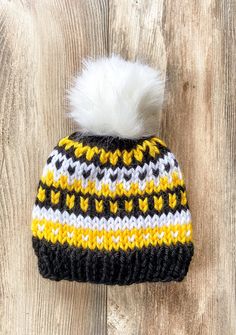 a black, yellow and white knitted hat with a pom - pom