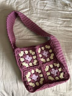 a pink crocheted purse sitting on top of a white bed next to a pillow