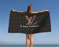 a woman is standing on the beach holding a louis vuitton towel