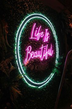 a neon sign that says life is beautiful in front of a wall with plants on it