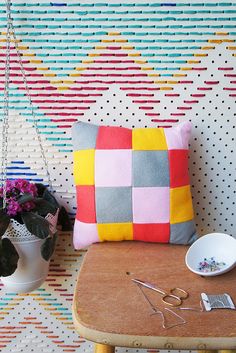 a wooden table topped with a bowl of flowers next to a wall covered in multicolored squares