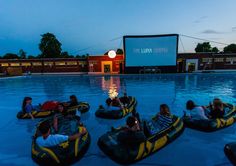 people are riding in bumper boats at the movies on the lawn area next to an empty swimming pool