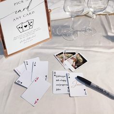 playing cards, pen and wine glasses on a white table cloth with an easel