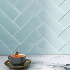 a coffee cup with saucer and spoon sitting on a marble countertop in front of a blue tiled wall