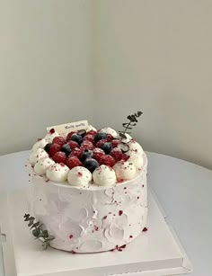 a white cake topped with berries and whipped cream on top of a book next to a plant