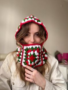 a woman wearing a red and green crocheted hat with flowers on it's face