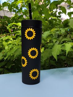 a black cup with yellow sunflowers painted on it and a straw in the middle