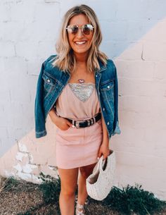 a woman wearing a pink skirt and denim jacket standing in front of a white brick wall