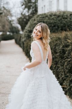 a woman in a white wedding dress is standing on the sidewalk and smiling at the camera