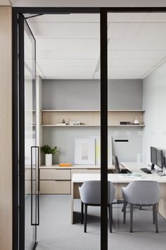 an office with two desks and chairs in front of a glass door that leads to the kitchen