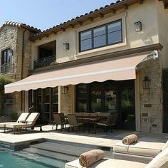 an outdoor swimming pool with lounge chairs and umbrellas next to the home's patio