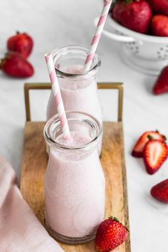 two strawberries sit next to each other on a wooden tray with milk and strawberries in the background