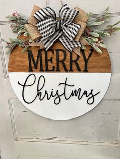 a merry christmas sign hanging on the front door with a bow and evergreens around it