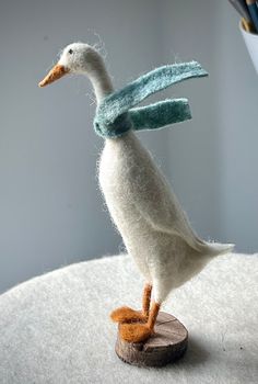 a needled white duck with blue scarf on it's head sitting on a piece of wood