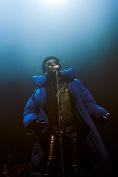 a man standing in front of a microphone wearing a blue jacket and black pants with his arms outstretched