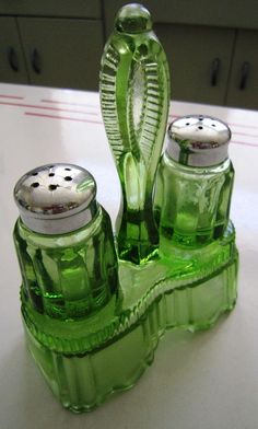 two green glass salt and pepper shakers sitting on a counter next to each other