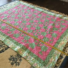 a pink and green quilt is laying on the floor next to a rug with a ruler in it