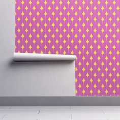 a pink and yellow wallpaper with geometric designs on the wall next to a roll of toilet paper