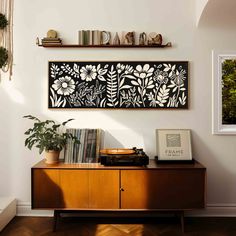 a wooden cabinet sitting next to a wall with pictures on it and plants in the corner