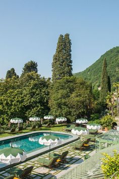 an outdoor swimming pool surrounded by trees and lawn chairs with umbrellas on the tables