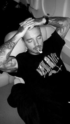 a man with tattoos on his arm and hand resting on the back of a couch