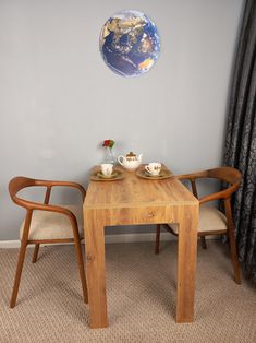 two chairs and a table with tea cups on it in front of a wall hanging