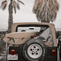 an old jeep with a surfboard strapped to the back in front of palm trees