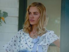 a woman with blonde hair standing in front of a window wearing a white shirt and blue bow tie