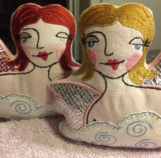 two hand sewn angels sitting on top of a pink blanket