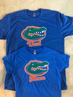 "This is a 100% cotton shirt. Some shrinkage may occur after washing. Please refer to the size charts for more information. Please specify in the customization field if the shirt should say Mom or Dad. If ordering more than one, please specify by size. Other customization/names are available, but the name would be below the Gator logo. Message me and I can send you a picture of what it would look like prior to ordering. Want a jersey look with name and number on the back? Message me for details Cotton T-shirt With Letter Print For Fans, Cotton Fan Apparel Shirt With Letter Print, Fan Apparel Short Sleeve Tops For Father's Day, Fan Apparel Cotton Shirt With Team Name, Father's Day Fan Apparel Short Sleeve Tops, Casual Cotton T-shirt For Fans, Casual Tops For Game Day On Father's Day, Basic Cotton T-shirt For Fan Merchandise, Short Sleeve Cotton Shirt With Team Name