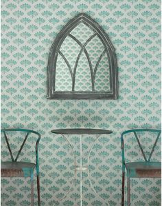 two chairs and a table in front of a wallpapered room with an arched window