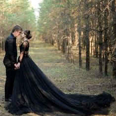 a man and woman dressed in black standing next to each other on a forest path